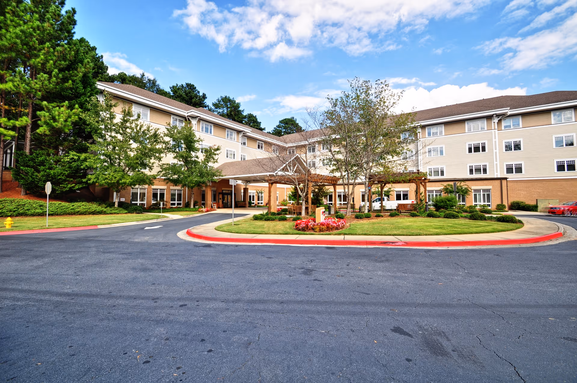 Front exterior of a multi-story senior living building with a circular driveway and landscaped entrance.