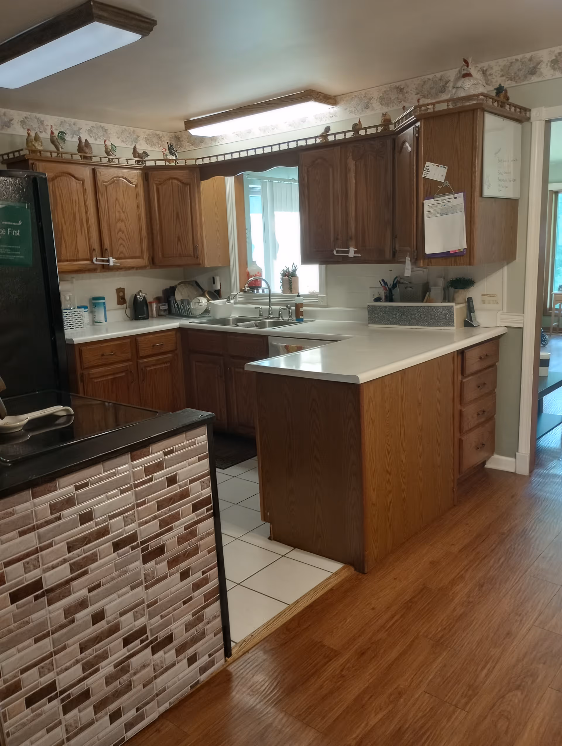 Kitchen with oak cabinets, white countertops and a sink under a window, plus a small island with a tiled end panel.