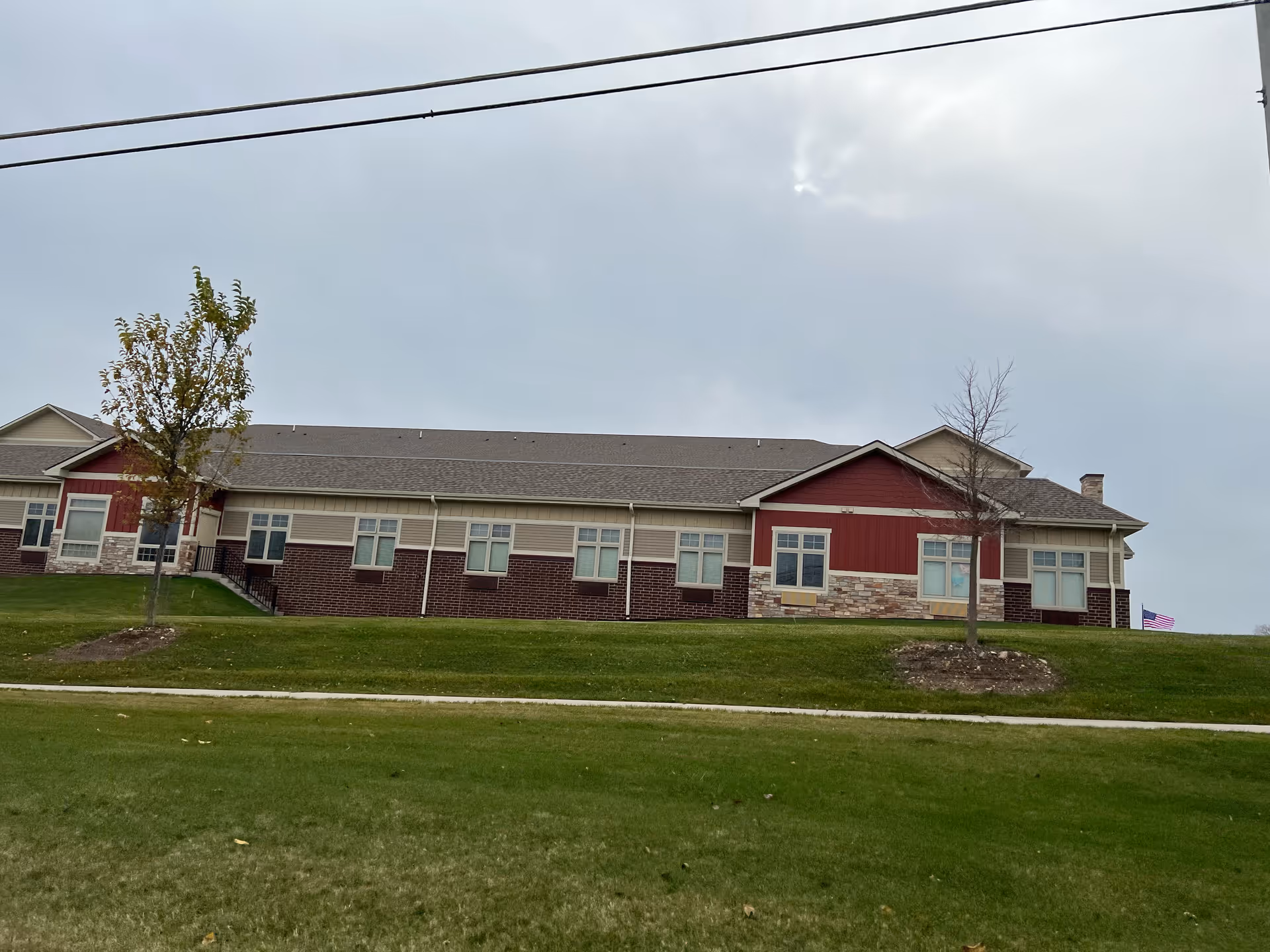 Single-story brick-and-siding building with multiple windows on a grassy lawn under a cloudy sky.