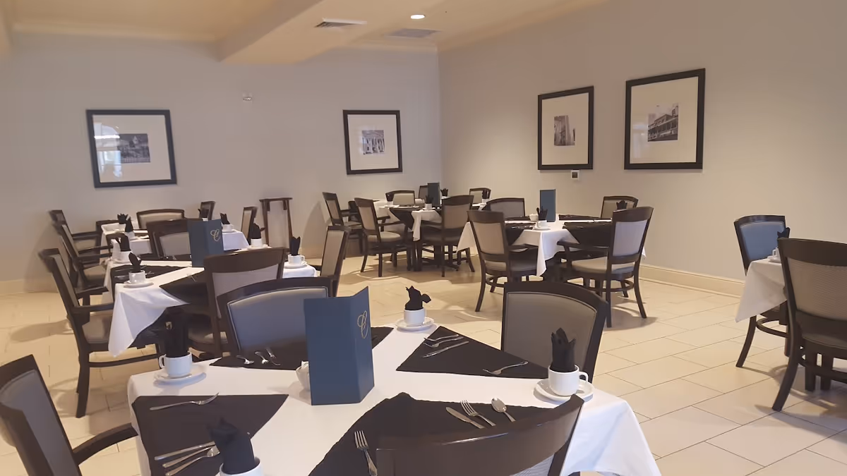 Dining room with multiple tables set with white tablecloths, black napkins, menus, and chairs.
