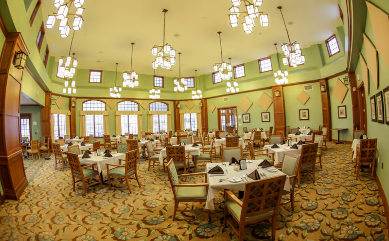 Spacious dining room with multiple set tables, high ceilings, pendant lights, and patterned carpet.