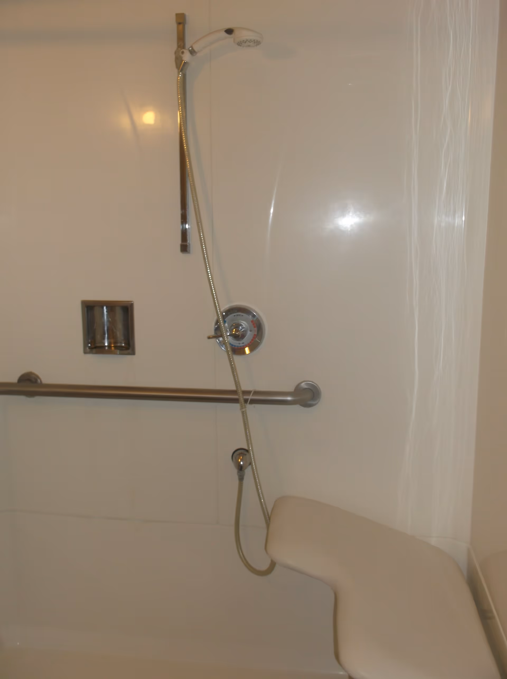 Shower stall with a handheld showerhead, stainless grab bar, recessed soap niche, and a built-in shower seat.