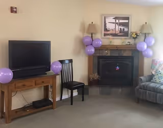 Living room with TV on a wooden stand, fireplace, and purple balloons around mantel.