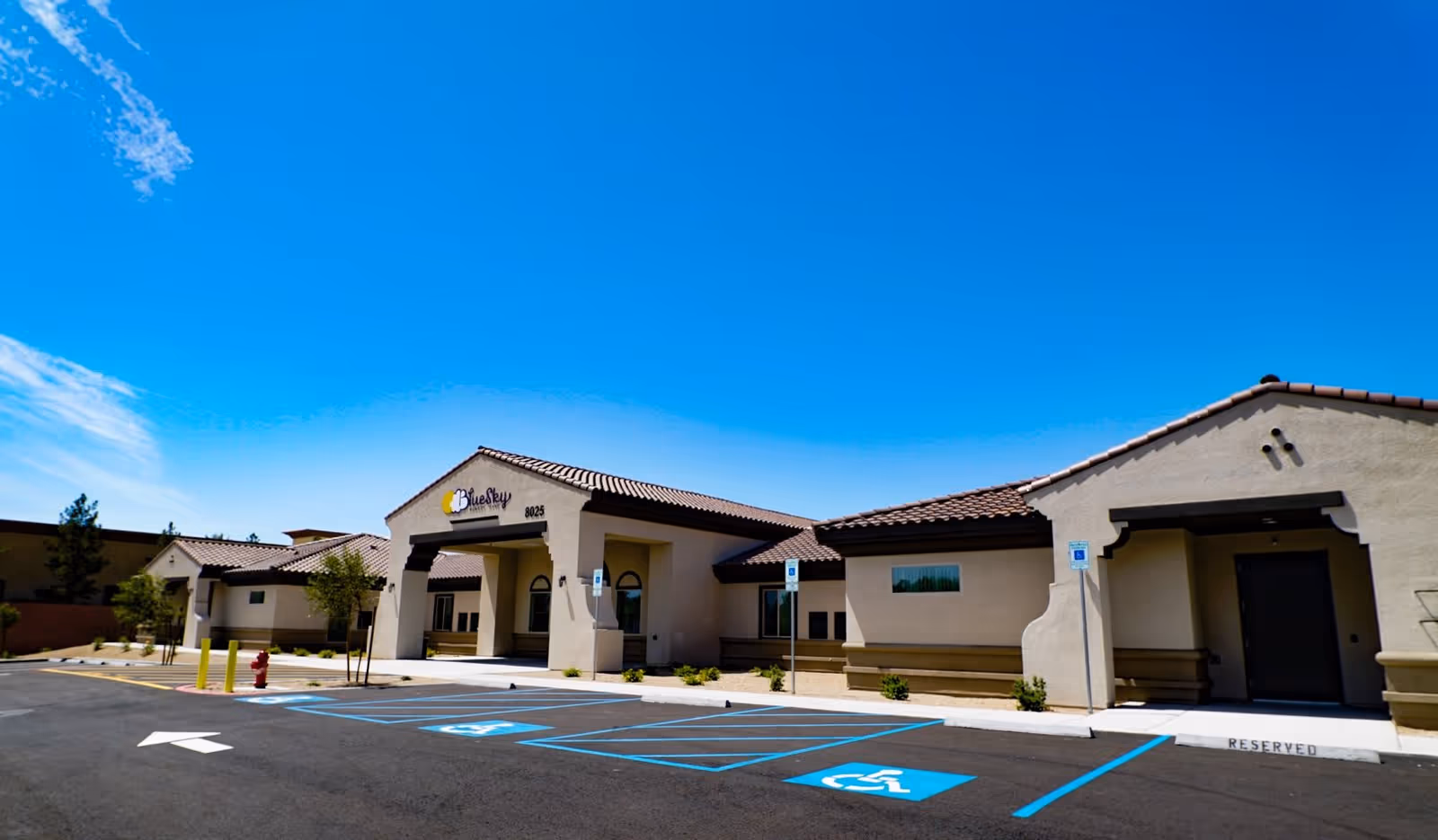 Exterior view of Blue Sky Memory Care facility with a clear blue sky, handicap parking spaces, and a reserved parking spot in front of the building entrance.