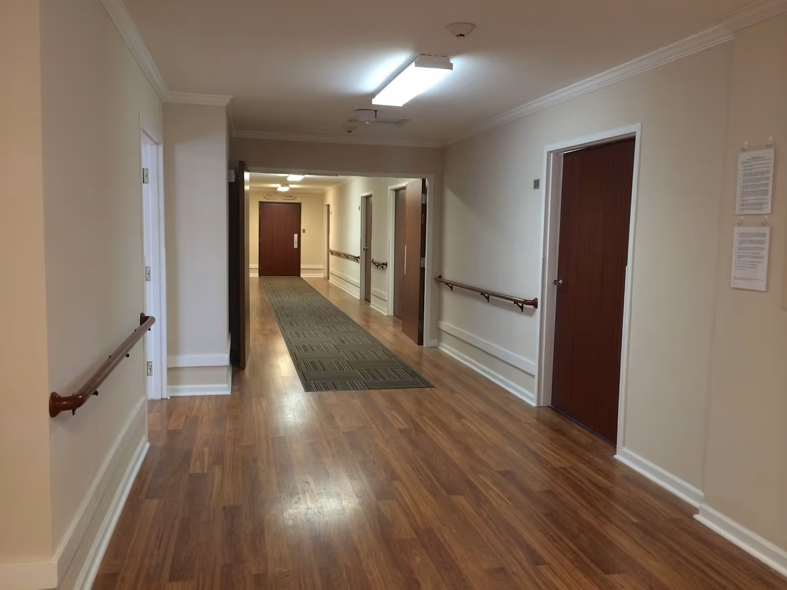 Long interior hallway with wood flooring, handrails along the walls, and several closed doors leading to rooms.
