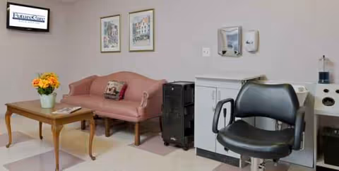 Pastel lounge with a pink sofa, coffee table with flowers, white cabinetry, and a black chair