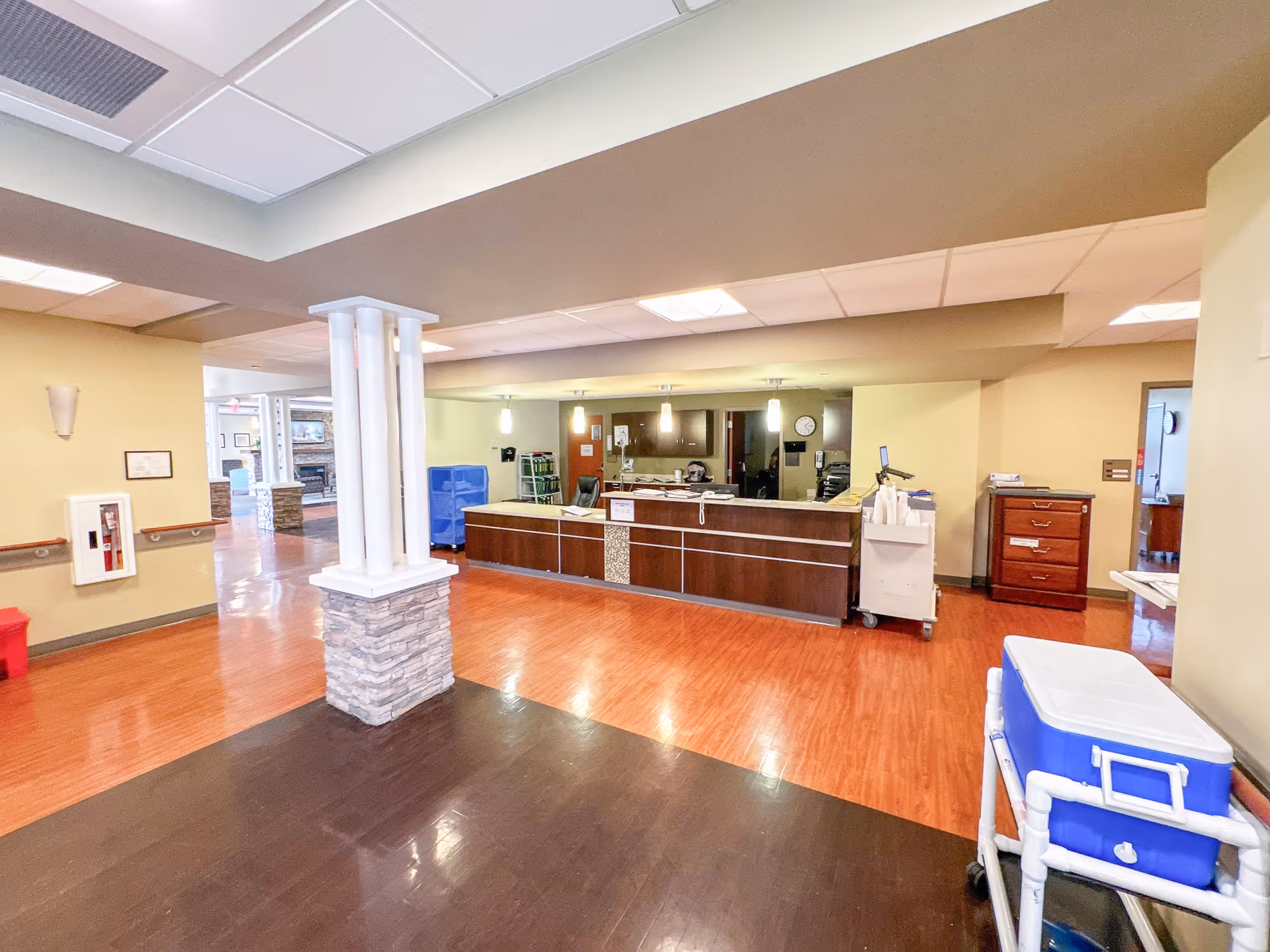 Spacious interior reception area with a central desk, decorative columns, wood floors and medical carts.