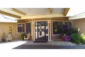 Entrance to Lakeside Assisted Living with glass doors, beige exterior, chairs, and blooming flowers.
