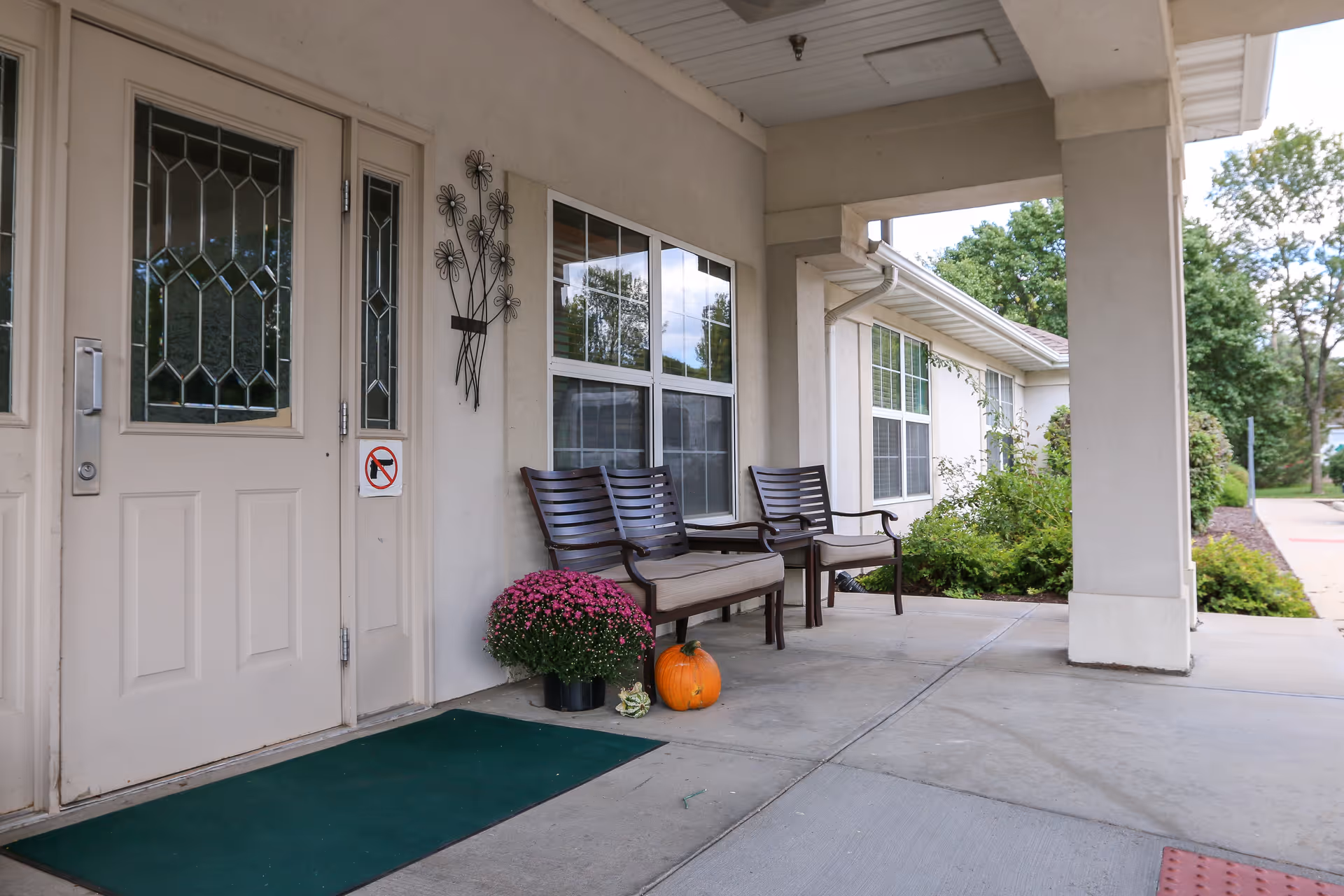 Covered front entrance with seating, potted mums and a pumpkin beside double doors.