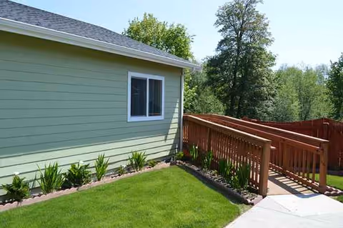 Side view of a green building exterior with a wooden deck and railing.
