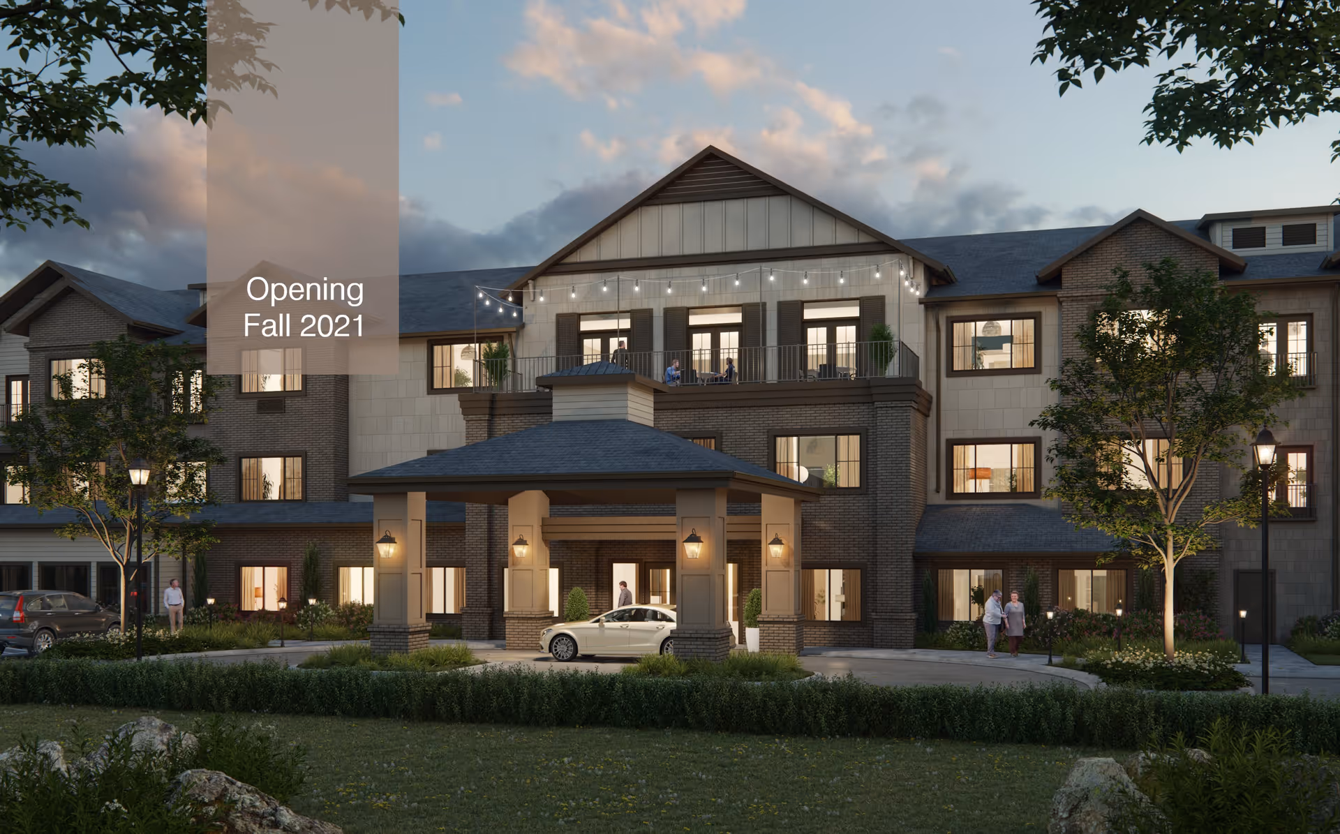 Exterior view of a three-story senior living facility building at dusk with warm lights glowing from the windows. The building features a covered entrance with columns and lantern-style lights. There are a few people walking and standing near the entrance and on the balcony above. Trees and landscaped greenery surround the building. Text overlay reads 'Opening Fall 2021'.