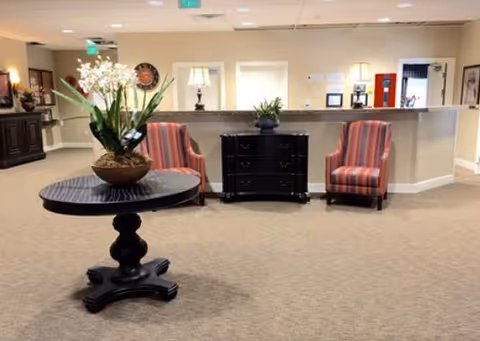 Reception lobby with a round table holding an orchid arrangement, two striped armchairs, and a reception desk in the background.