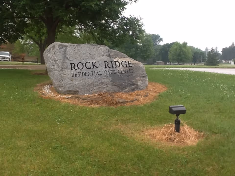 Large engraved stone reading 'Rock Ridge Residential Care Center' on a grassy lawn with trees and a spotlight.