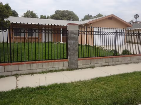 Exterior view of a single-story building with a black iron fence and green lawn.