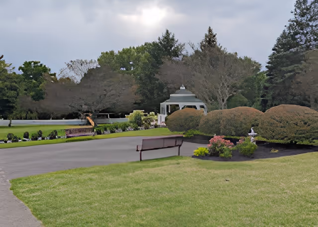 Manicured outdoor garden with a gazebo, benches, and trimmed bushes on a lawn.