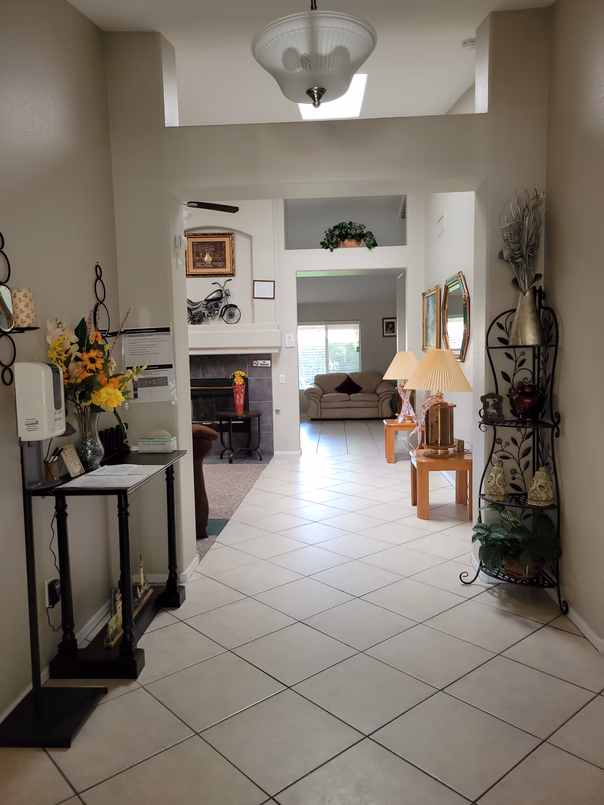 Tiled entry hallway leading to a furnished common area with couches, a fireplace, side tables, lamps, and decorative shelving.