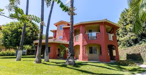 Red two-story building with arches and balconies sits on a green lawn.