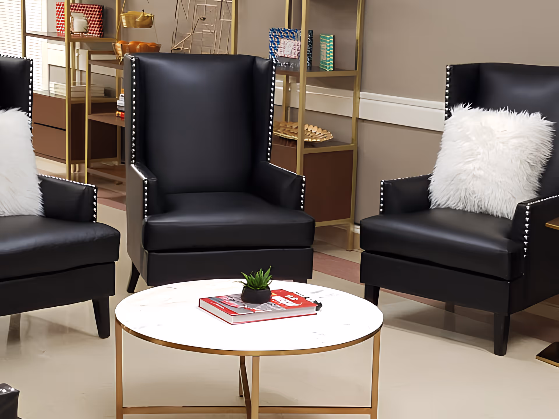 Three black leather armchairs with white fluffy pillows around a round marble-top coffee table holding a small plant and a book in a lounge area.