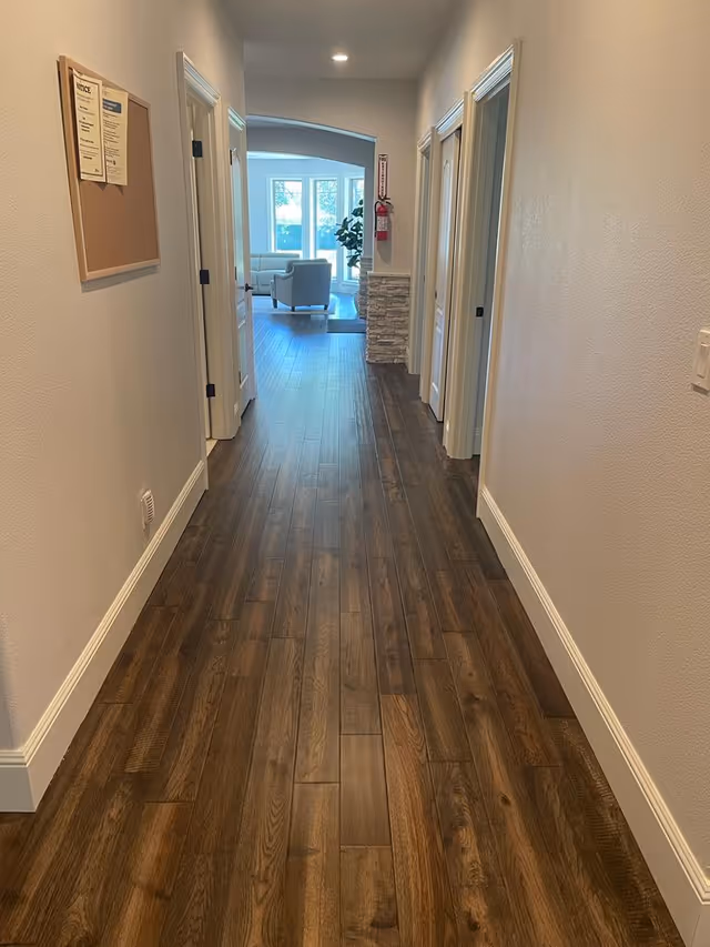 Long interior hallway with dark wood floors, doors on both sides, and a seating area visible at the far end.