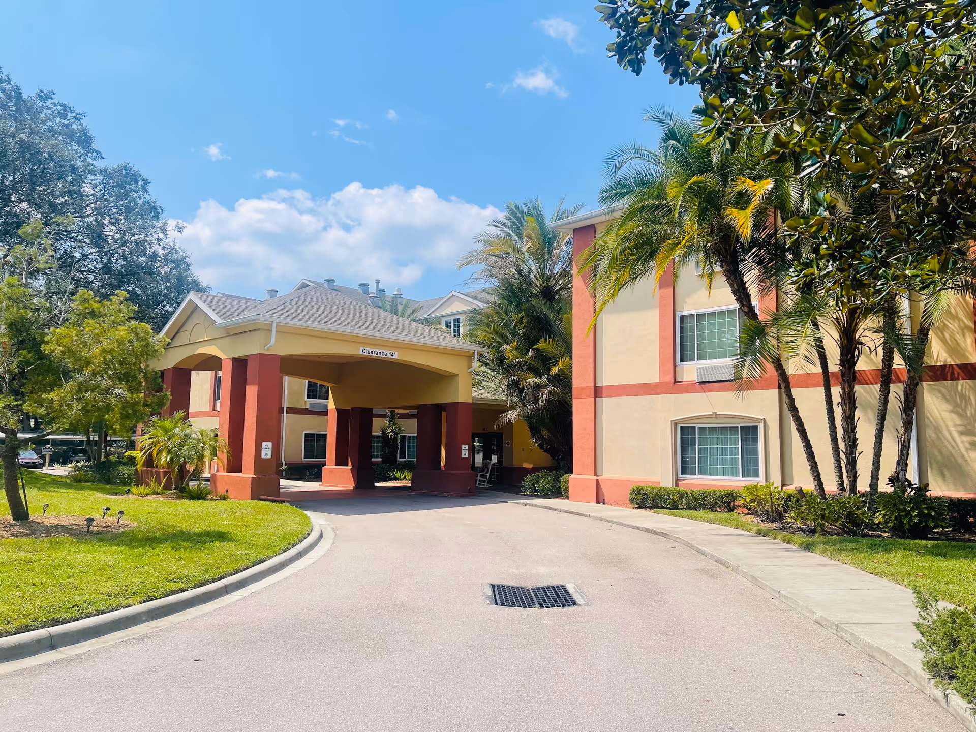 Front entrance and porte-cochère of a multi-story senior living building with palm trees and a curved driveway.