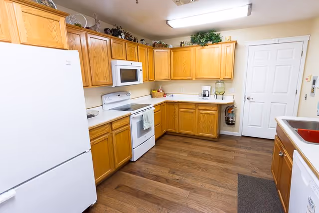 Well-lit communal kitchen with oak cabinets, white appliances, and wood flooring.