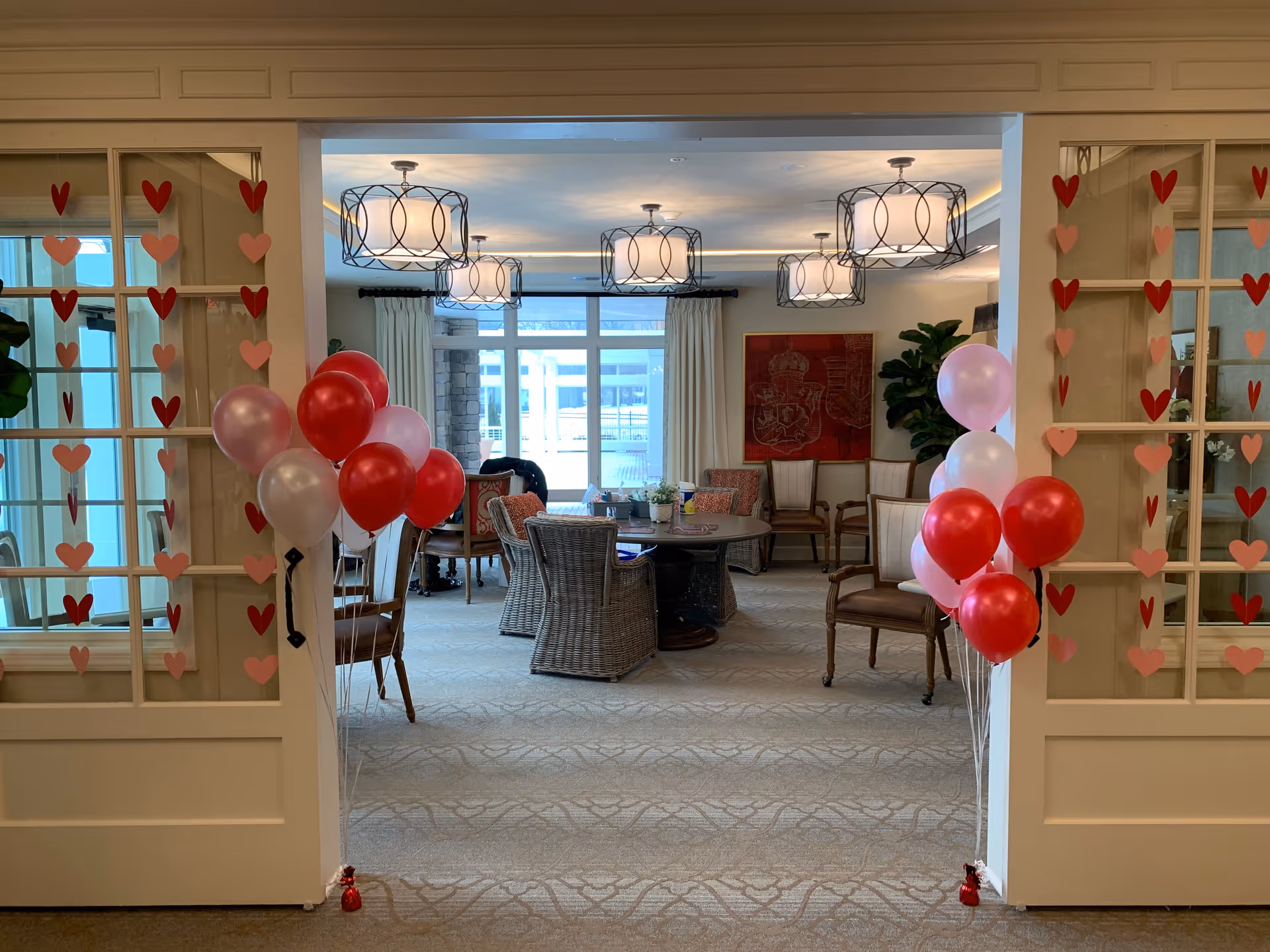Entrance to a decorated common room with balloons, heart cutouts on the glass doors, and a round table surrounded by chairs.