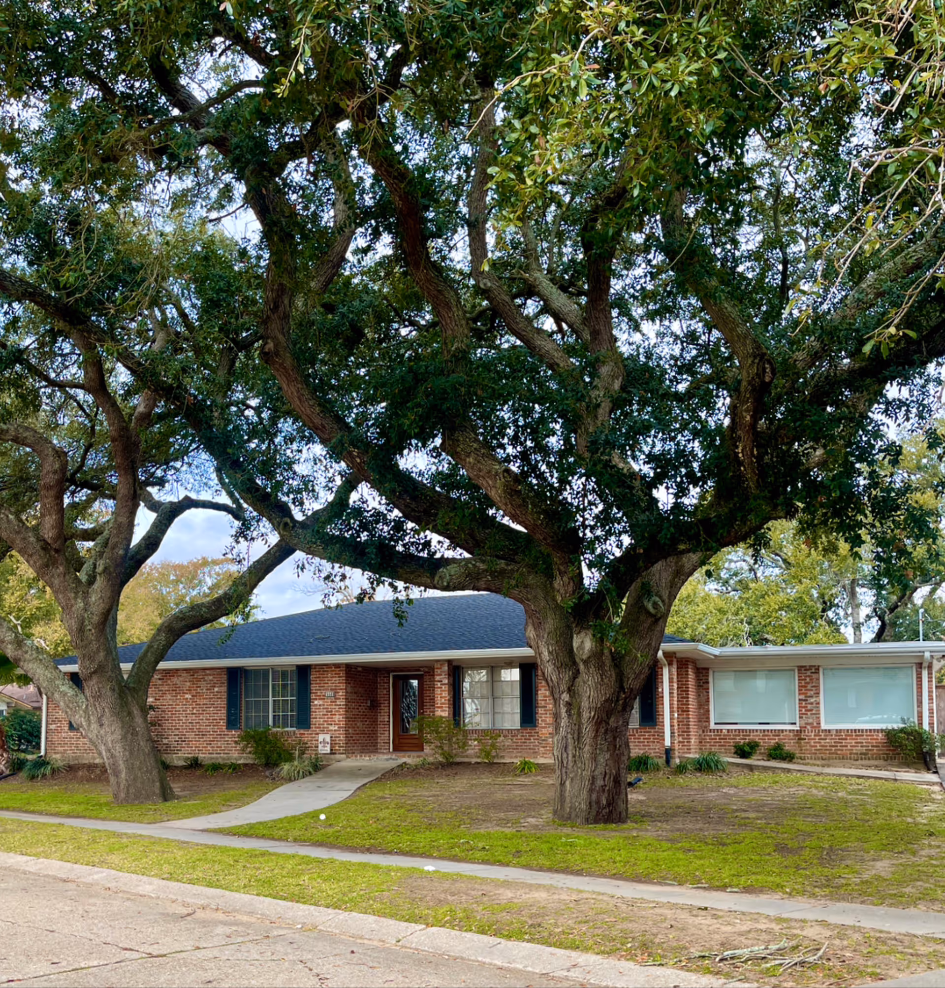 Single-story brick building with a front entrance and large oak trees in the yard.
