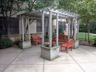 Outdoor courtyard with a pergola, red chairs, potted plants, and a concrete patio.