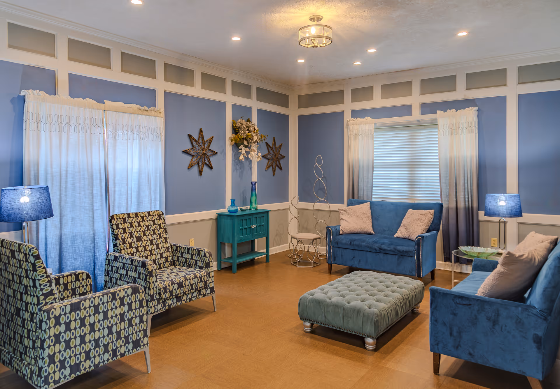 Cozy blue-themed common lounge with patterned armchairs, velvet sofas, a tufted ottoman and decorative accents.