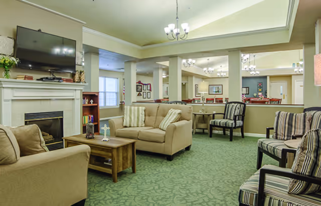 Comfortable common living room with sofas, armchairs, a fireplace and TV, with a dining area visible in the background.