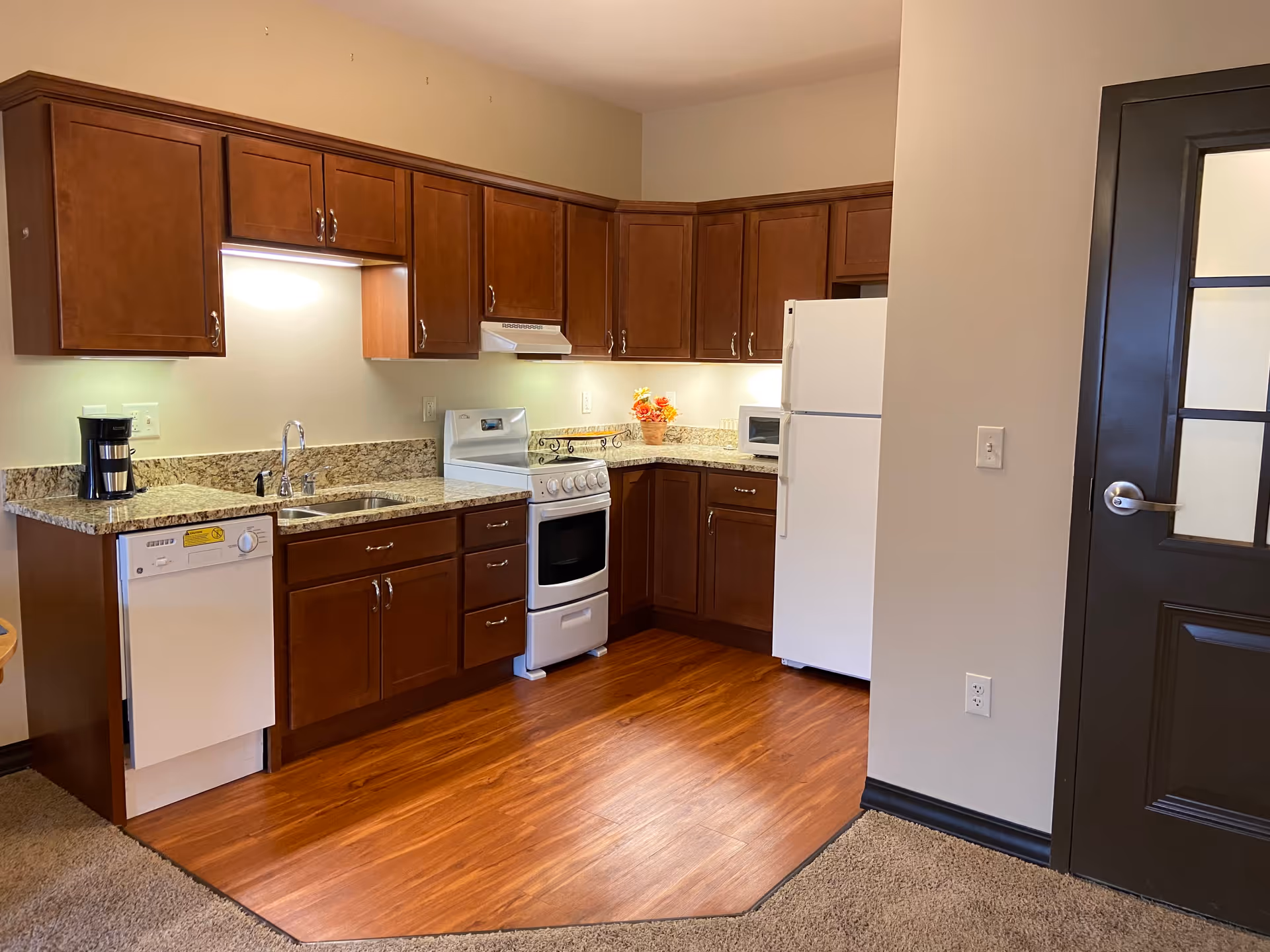 Small kitchen with wood cabinets, granite countertops, white appliances, and wood-look flooring.