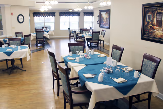 Dining room with several tables set with teal tablecloths, place settings, and chairs in a bright communal space.