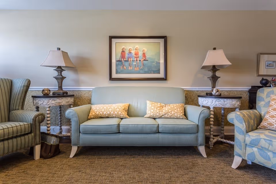 A cozy seating area with a light blue sofa flanked by patterned armchairs, decorative side tables with lamps, and a framed painting above.
