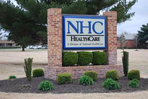 NHC HealthCare sign on brick pillars with manicured shrubs in front.