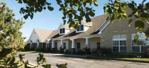 Brookdale Great Bend exterior with entrance, flag, and manicured shrubs on a sunny day