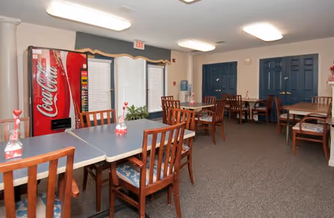Dining room with several tables and wooden chairs, a Coca-Cola vending machine against the wall, and blue double doors.