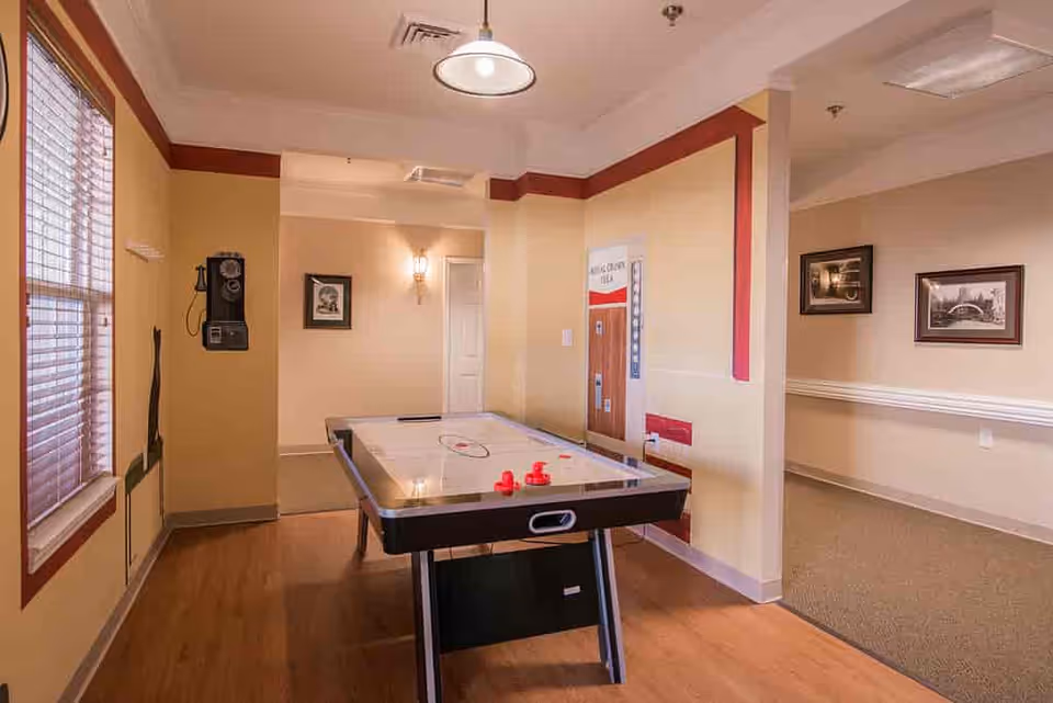 Interior common room featuring an air hockey table, wall-mounted phone and framed pictures by windows.