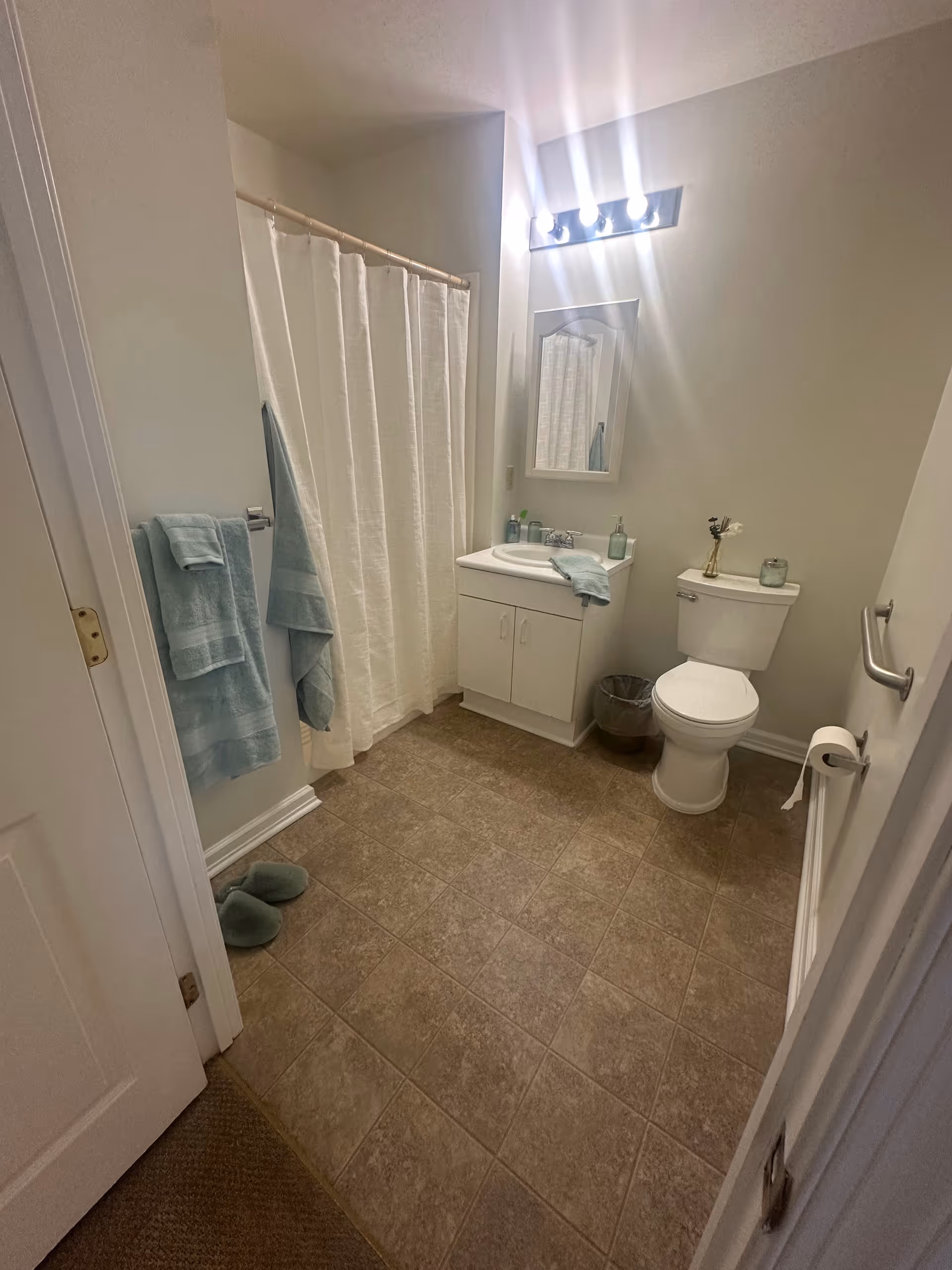 Bright bathroom showing a shower with a white curtain, a sink vanity with mirror, a toilet, and blue towels.