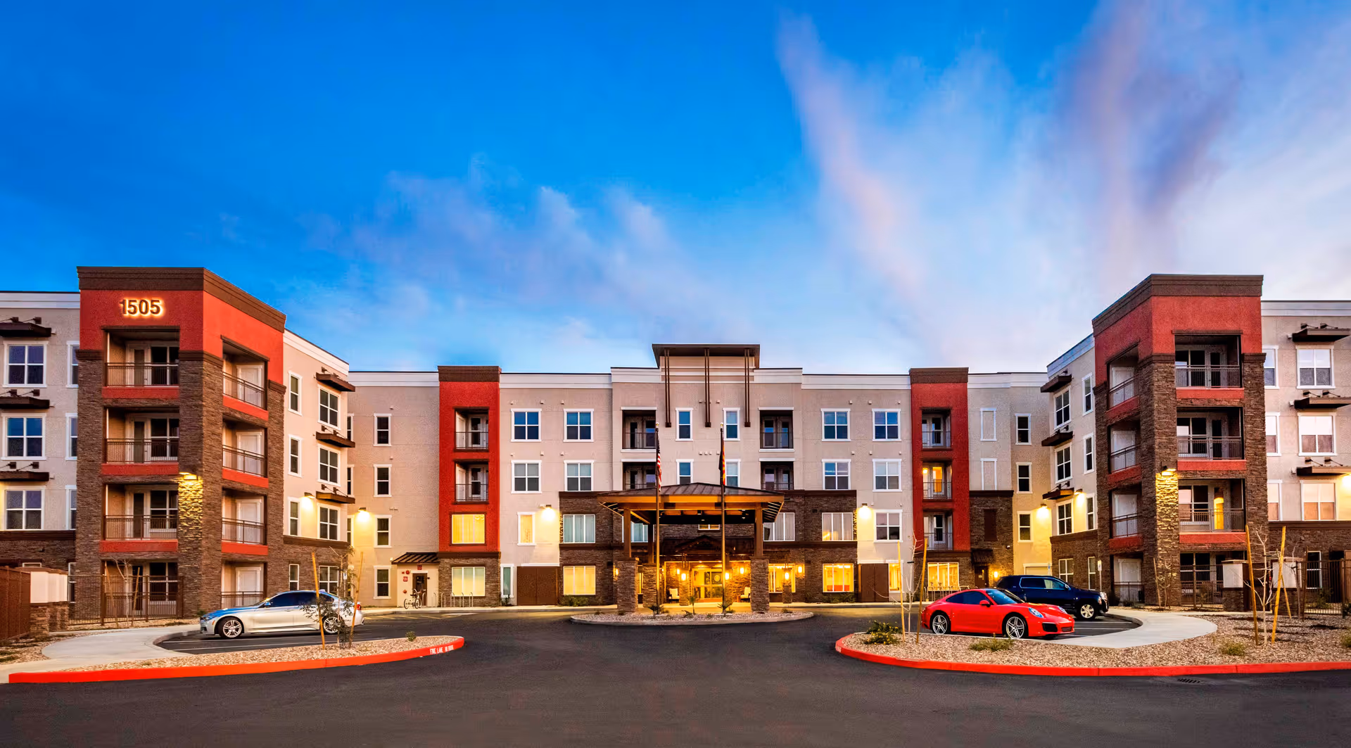 Exterior view of a modern multi-story senior living facility building named Verena at Gilbert during dusk, with a circular driveway and several parked cars in front.