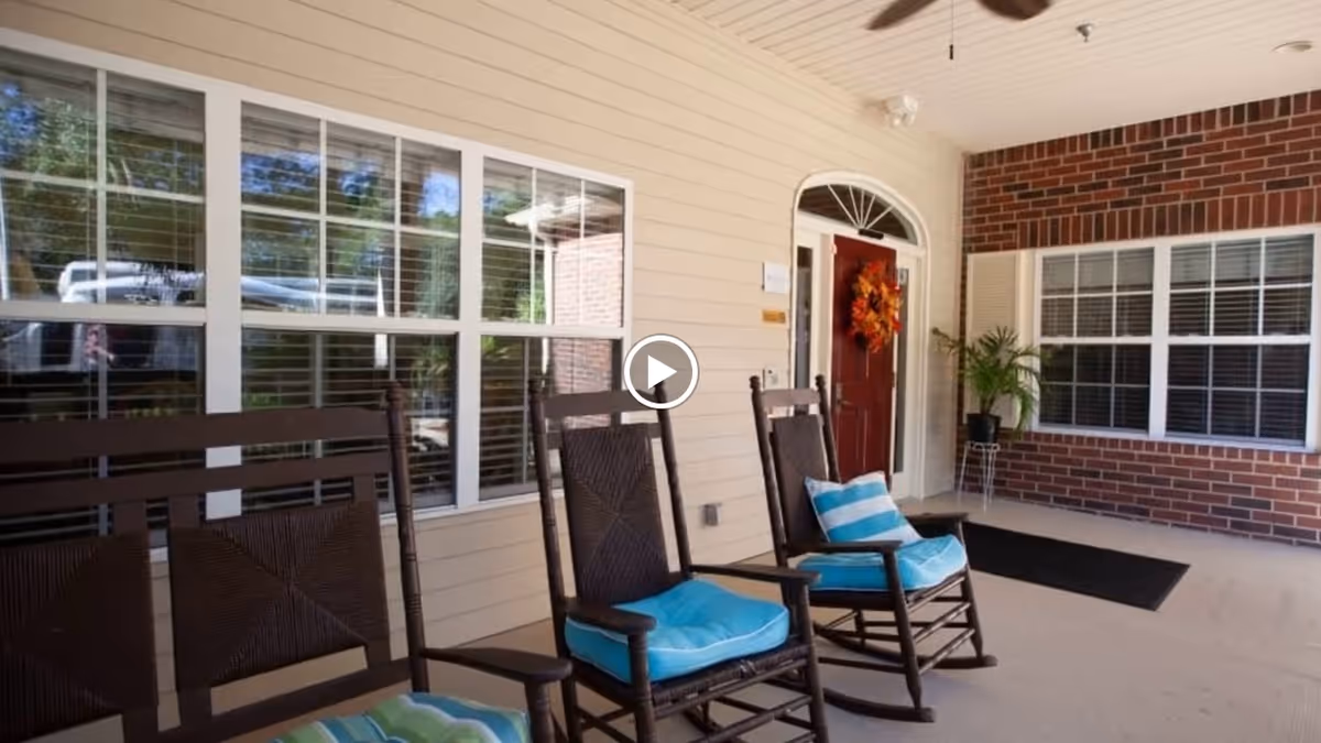 Covered front porch with wooden rocking chairs topped with blue cushions facing the entrance door decorated with a wreath.