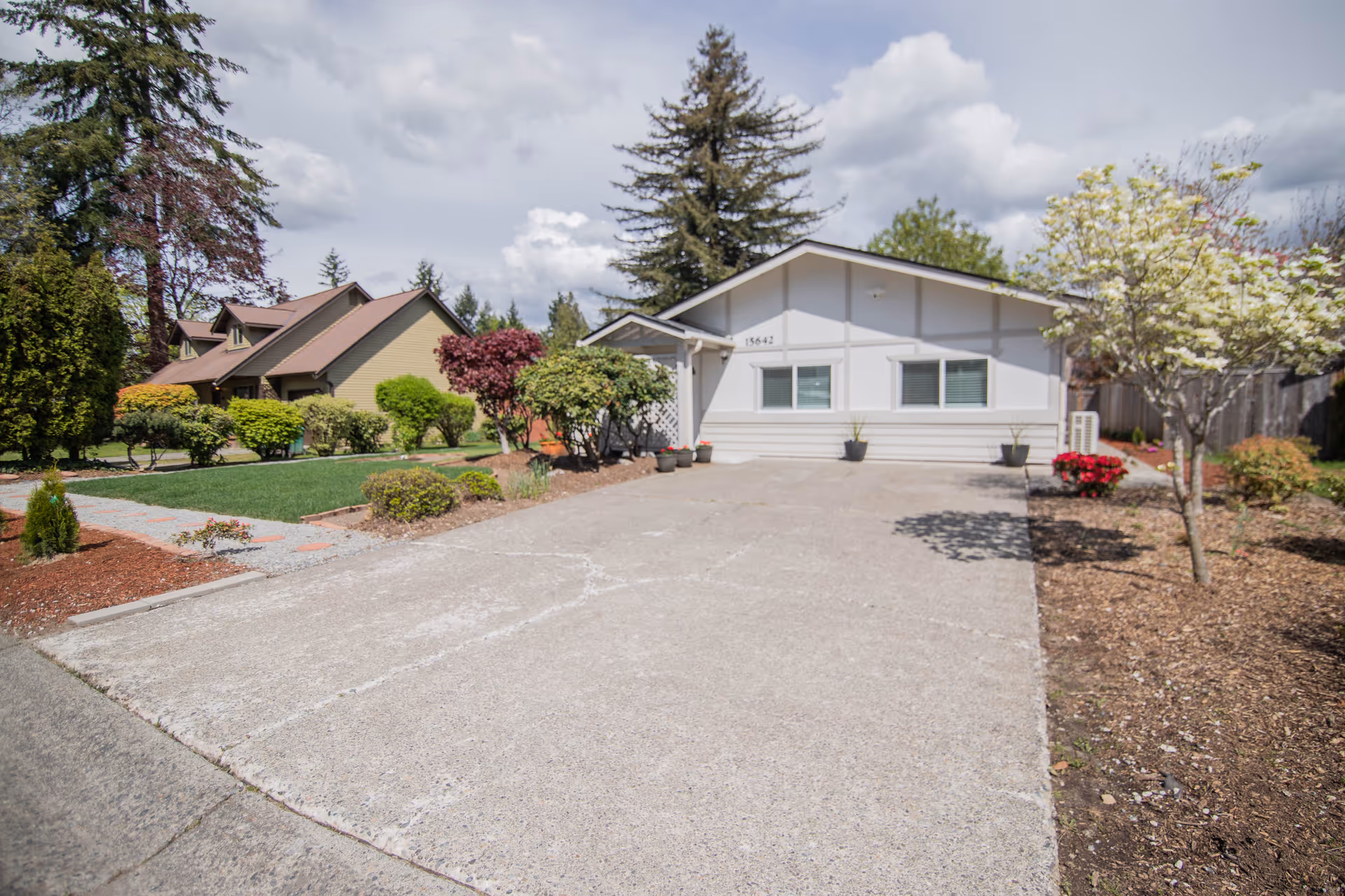Single-story light-colored house with a wide concrete driveway and landscaped front yard.