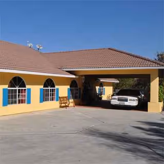 Yellow senior living facility with blue shutters, arched windows, and a carport with a parked car.