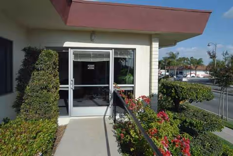 Exterior entrance to a medical facility with glass doors, shrubs, and flowering plants.
