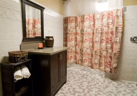 A bathroom with a dark vanity, mirror, towels, and a patterned shower curtain.