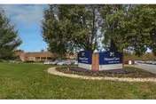 Exterior view of a skilled nursing and rehabilitation center with a landscaped entrance sign, parking lot, and trees.