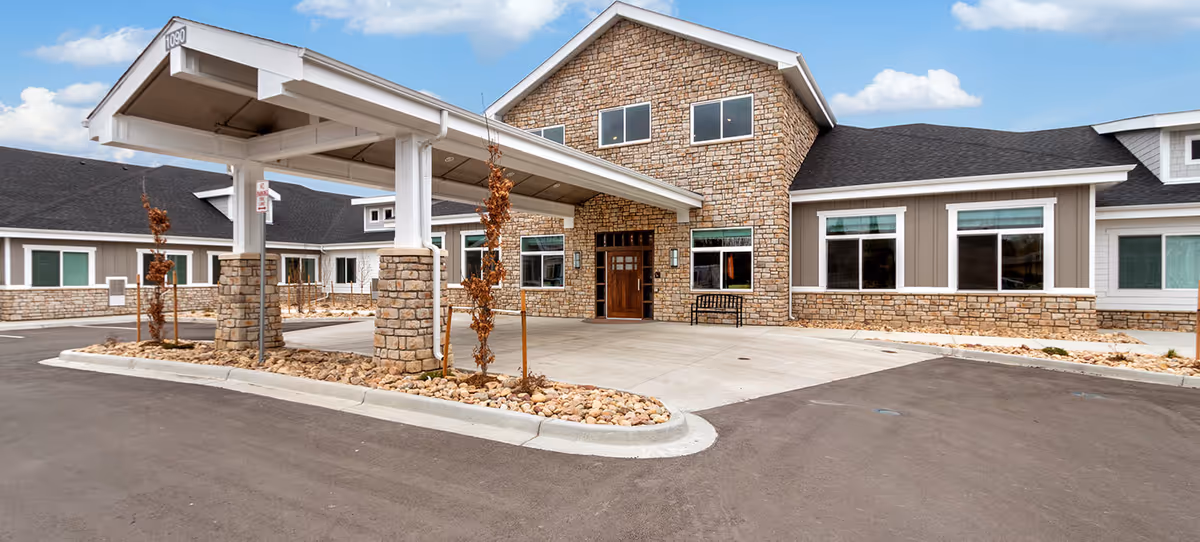 Front exterior of a senior living building with stone facade and a covered drop-off porte-cochere.