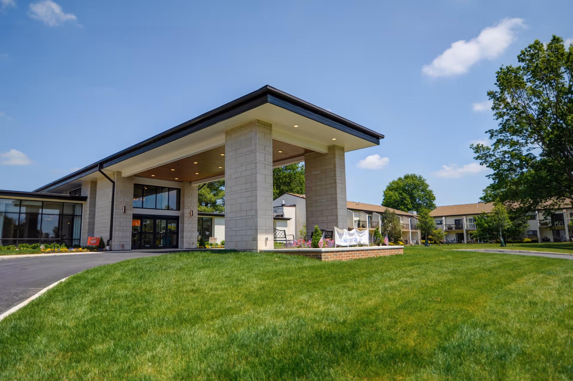 Modern senior living facility exterior featuring a porte-cochère, glass entry, and manicured lawn.