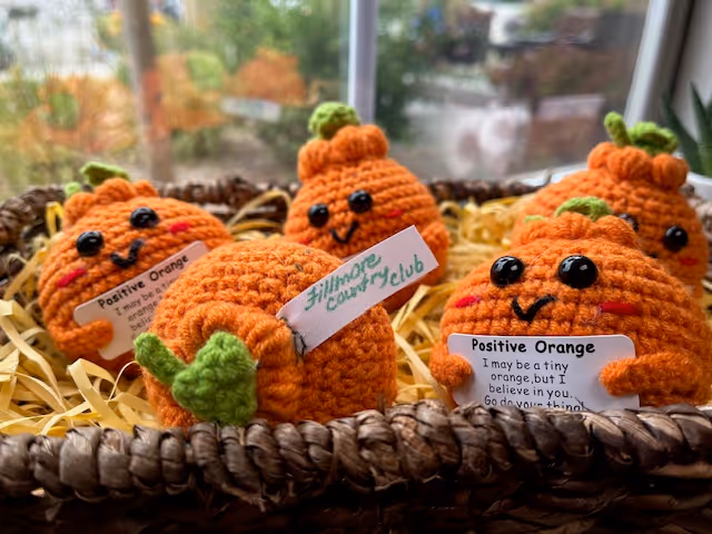 Handmade crocheted orange pumpkin decorations with smiling faces arranged in a woven basket on a windowsill.