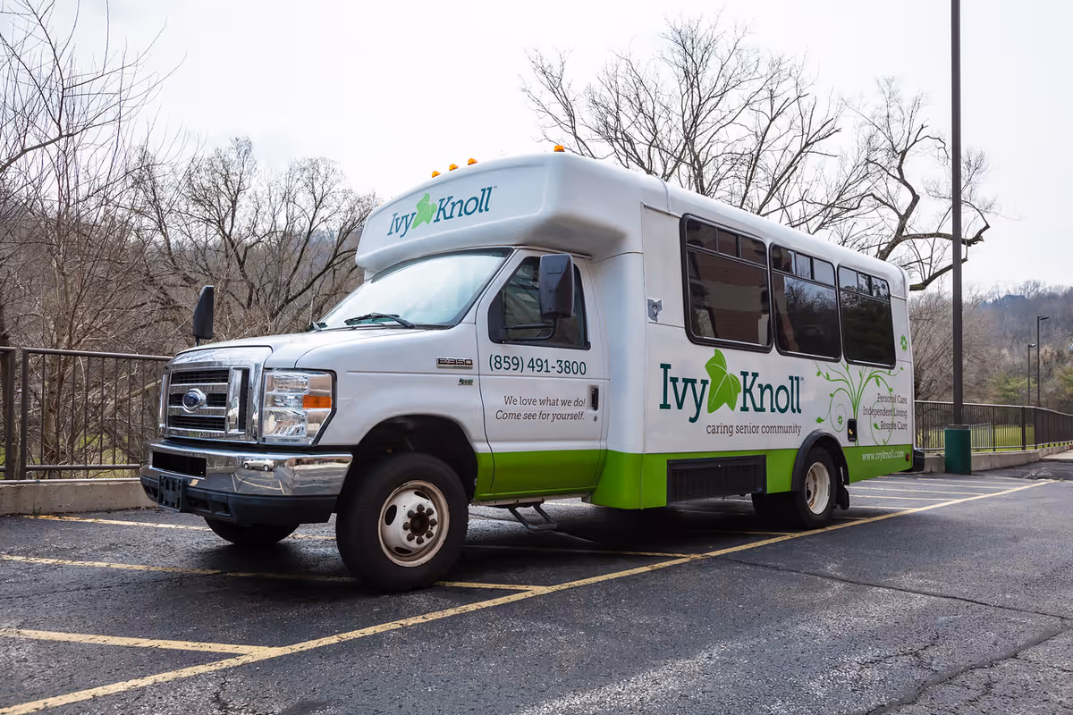 A white and green Ivy Knoll senior living shuttle bus parked in an outdoor lot.