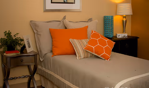 Single bed in a cozy bedroom with orange accent pillows, bedside tables and a lamp.